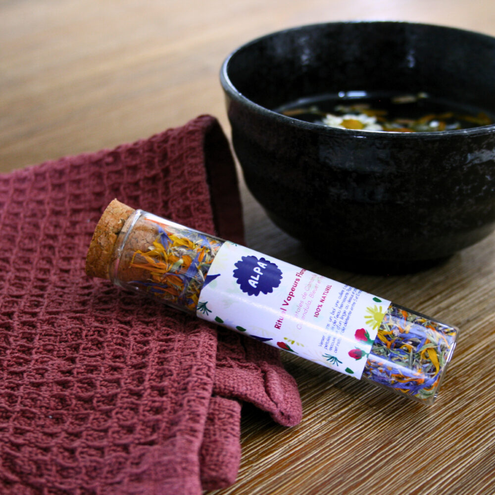 L'Inhalation avec des pétales de camomille, bleuet, thym et calendula, posée sur un linge pour l’inhalation, à côté d’un bol d’eau bouillante avec plantes, sur une table en bois, ambiance chaleureuse.