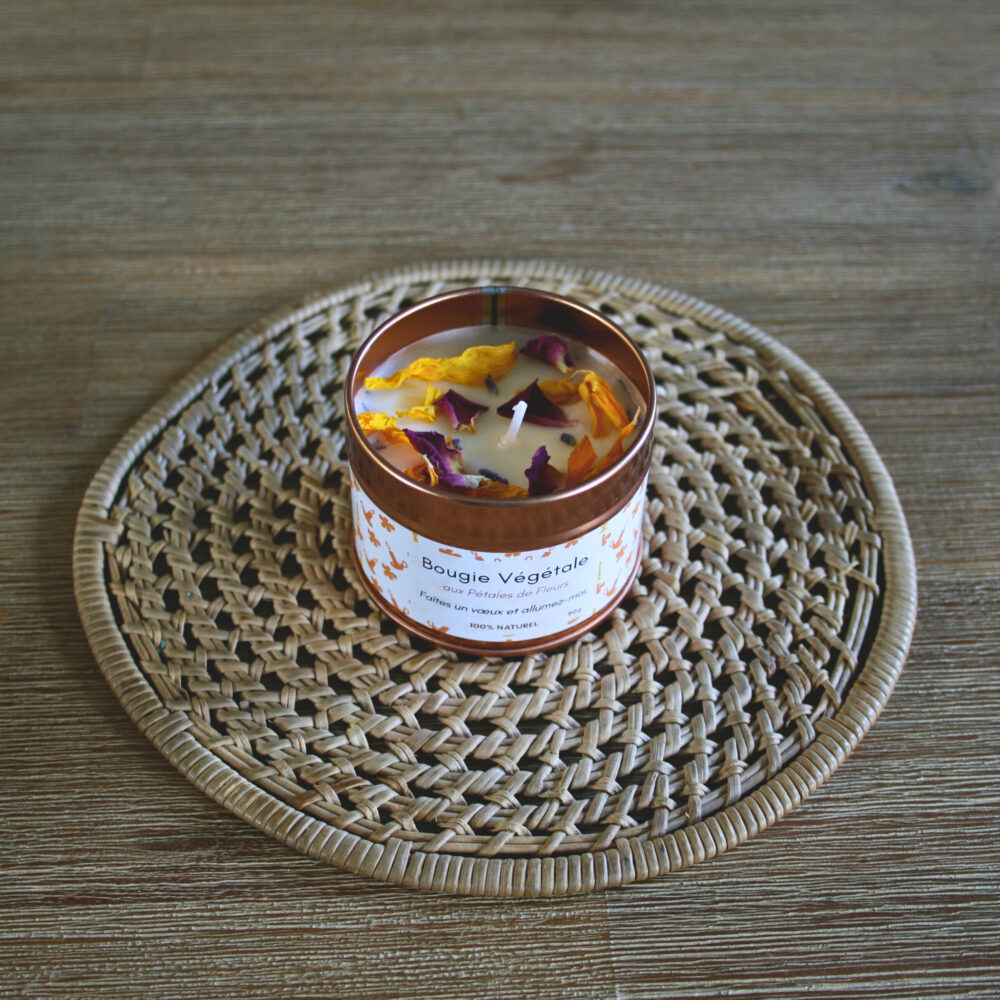 Bougie végétale dans un pot rond métallique, à base de cire de soja naturelle, ornée de pétales de fleurs, posée sur une table en bois.