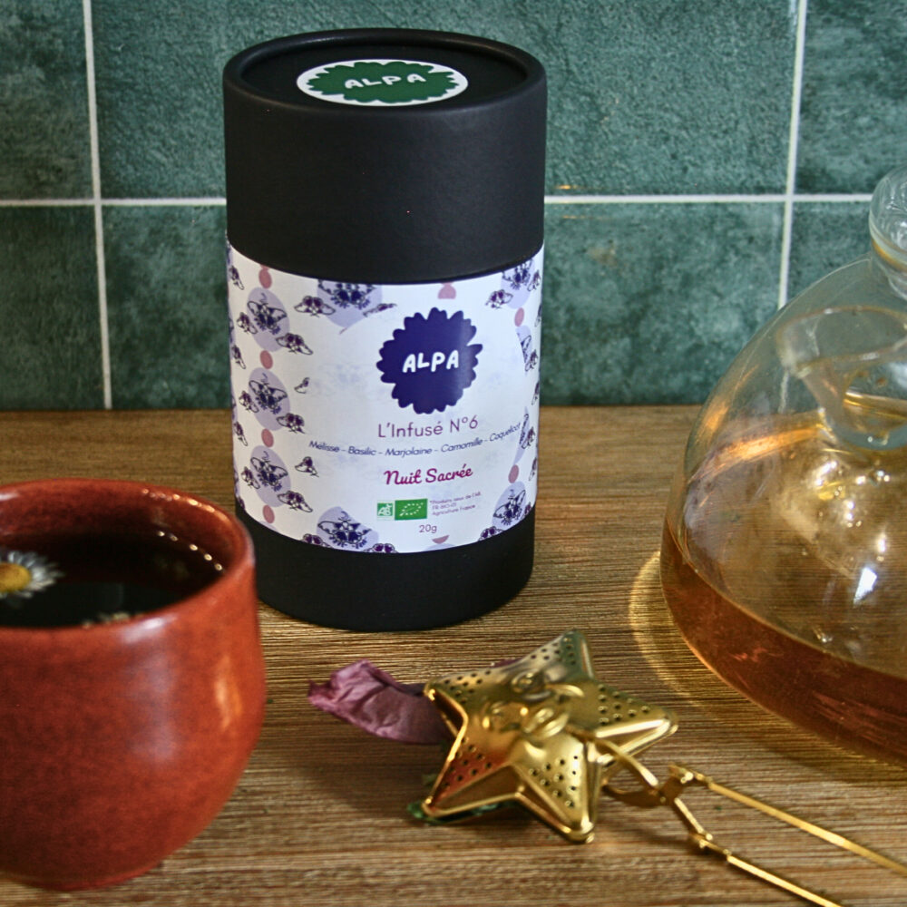 Infusé N°6 – Nuit Sacrée dans une tasse, avec une théière à côté et une boule à thé dorée en forme d’étoile, posés sur un plan de travail de cuisine, évoquant un moment de détente nocturne.